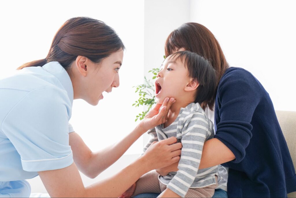 お母さんに抱っこされて口の中を見せる子ども
