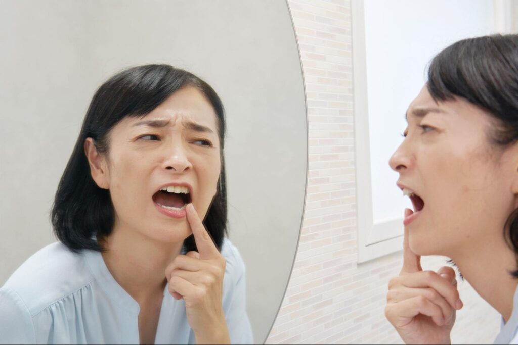 顔を歪めて鏡で口の中を見ている女性