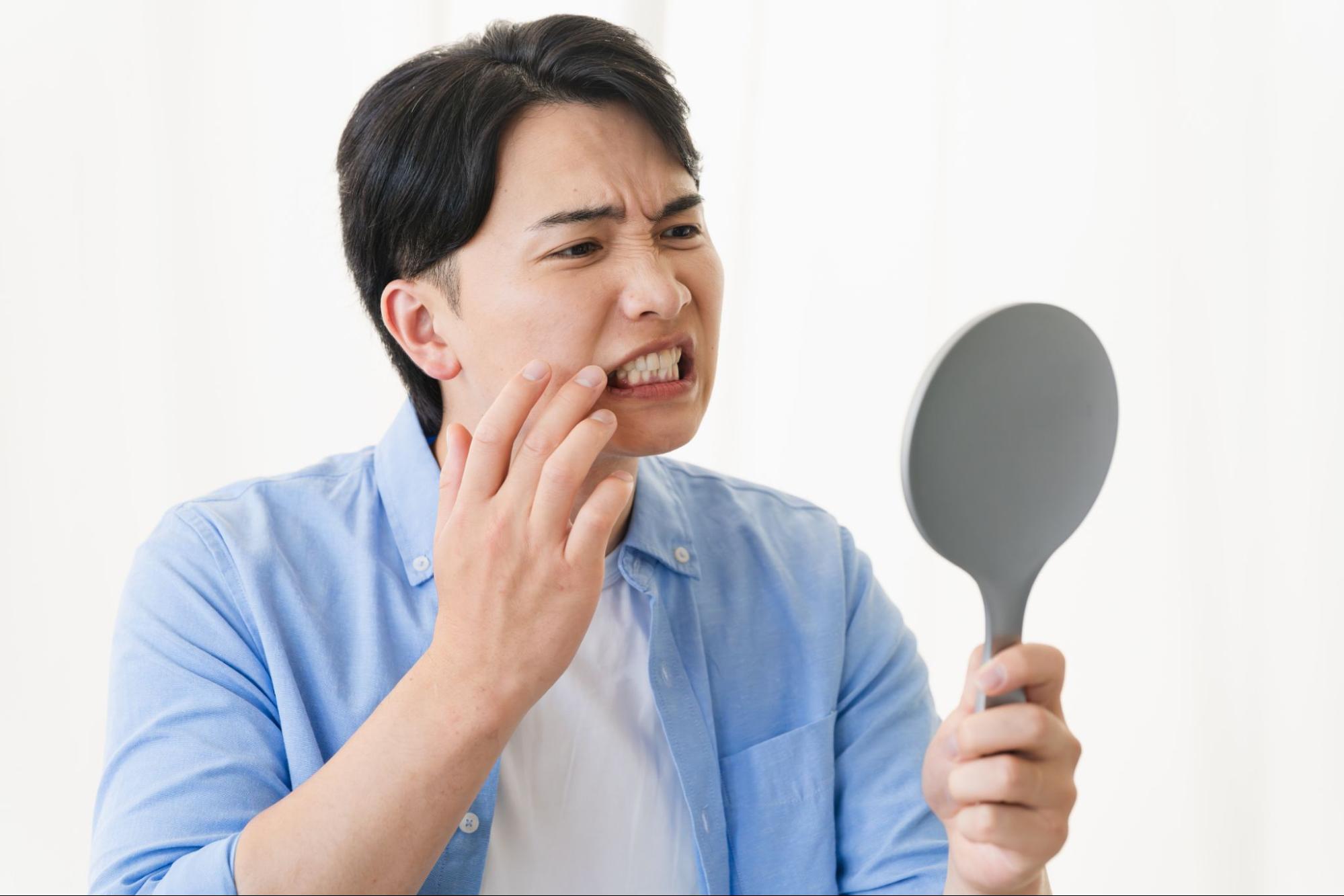 虫歯の痛みが気になって鏡を見る男性