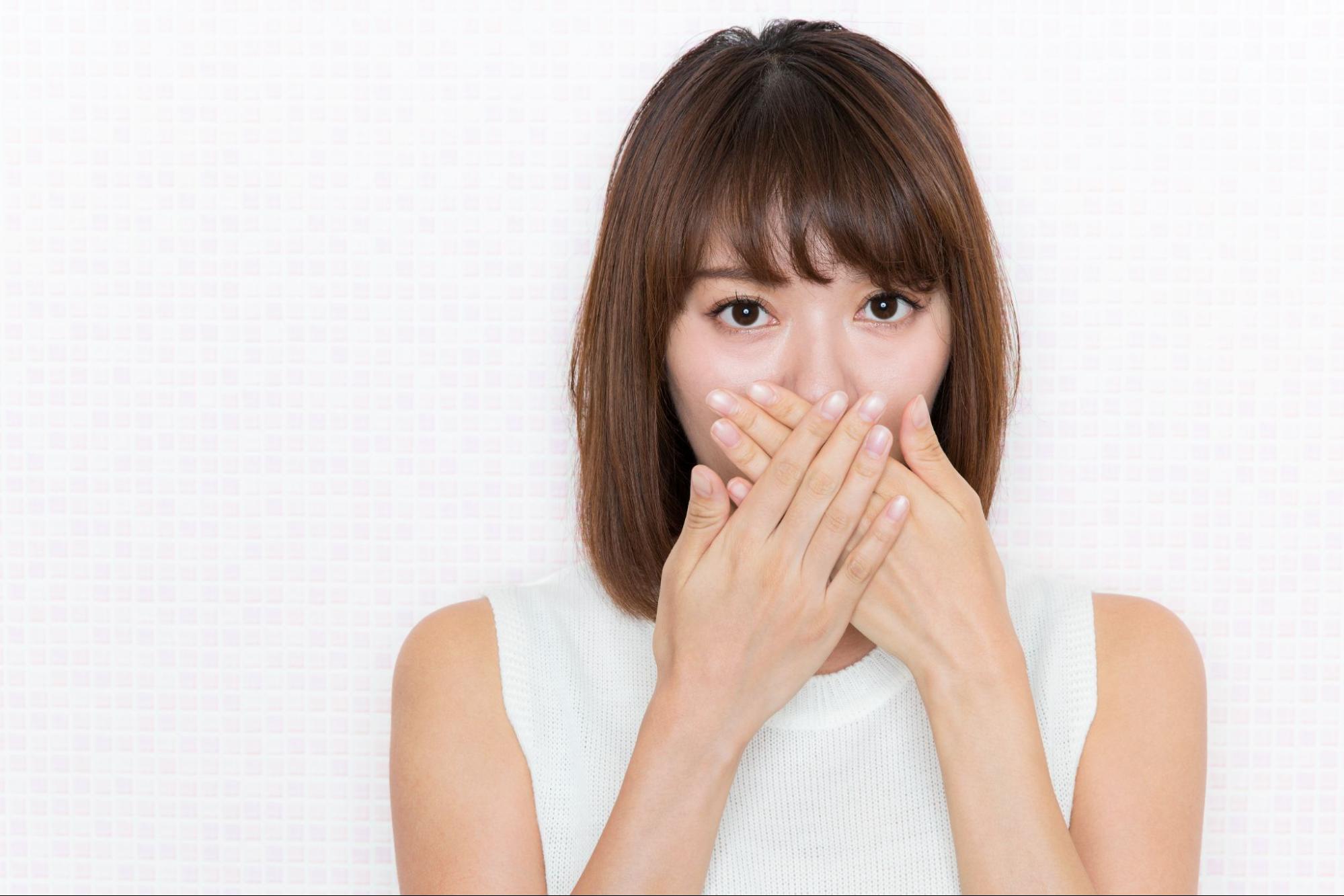虫歯による口臭が気になり口元に手を当てる女性
