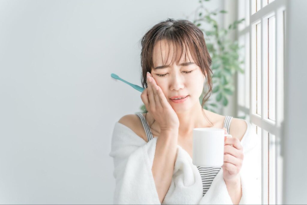 歯磨き中に生えかけの親知らずが痛み頬を押さえる女性